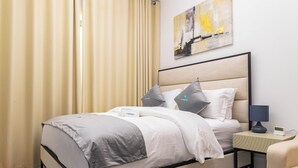 A neatly arranged hotel room with a bed, bedside table, and a chair. - Bloomfields Lavish STU in Oasis Masdar (Abu Dhabi)