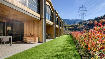 Ein modernes Gebäude mit Holzfassade, einer Terrasse mit Gartenmöbeln und einem gepflegten Rasen.