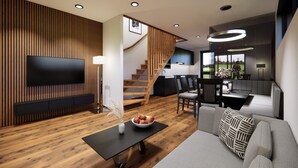 A modern living room with a flat-screen TV, wooden paneling, a staircase, a dining area, and a sofa with patterned cushions. - Bsundrix Wellness Tiny Vaya (Lorüns)