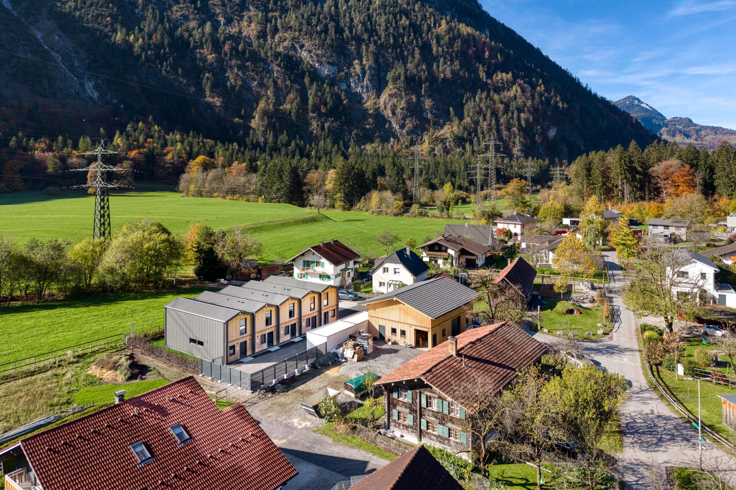 A residential area with houses, a green field, and mountains in the background.