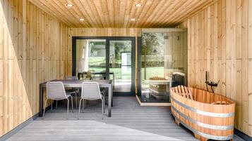 Un intérieur en bois comprenant un coin repas, un sauna et une porte vitrée donnant sur l’extérieur.