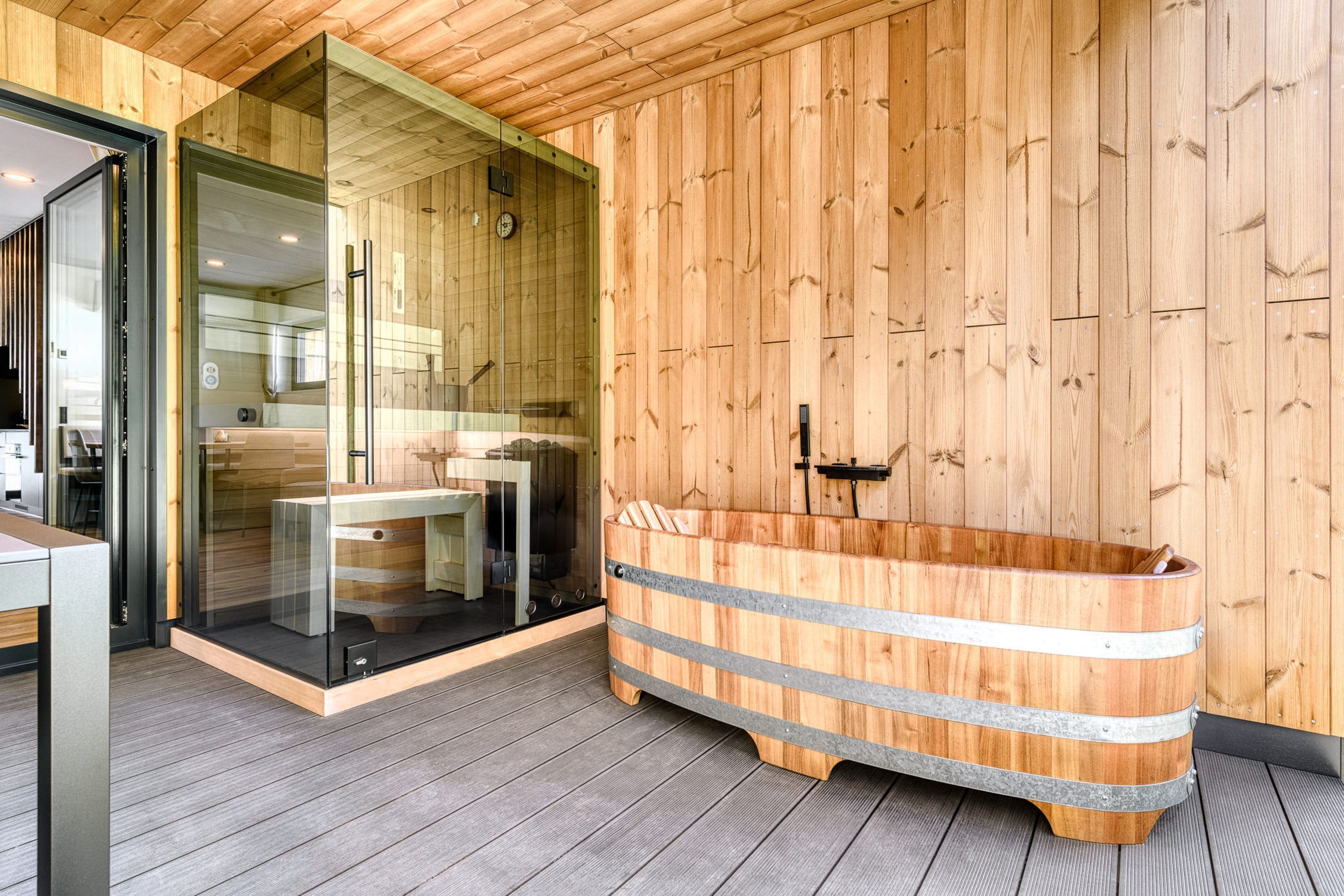 A wooden interior with a bathtub, a glass door leading to a bathroom, and a wooden floor.