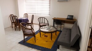 Een woonkamer met een eethoek, een bank, een rond bijzettafeltje en een laptop op een bureau.