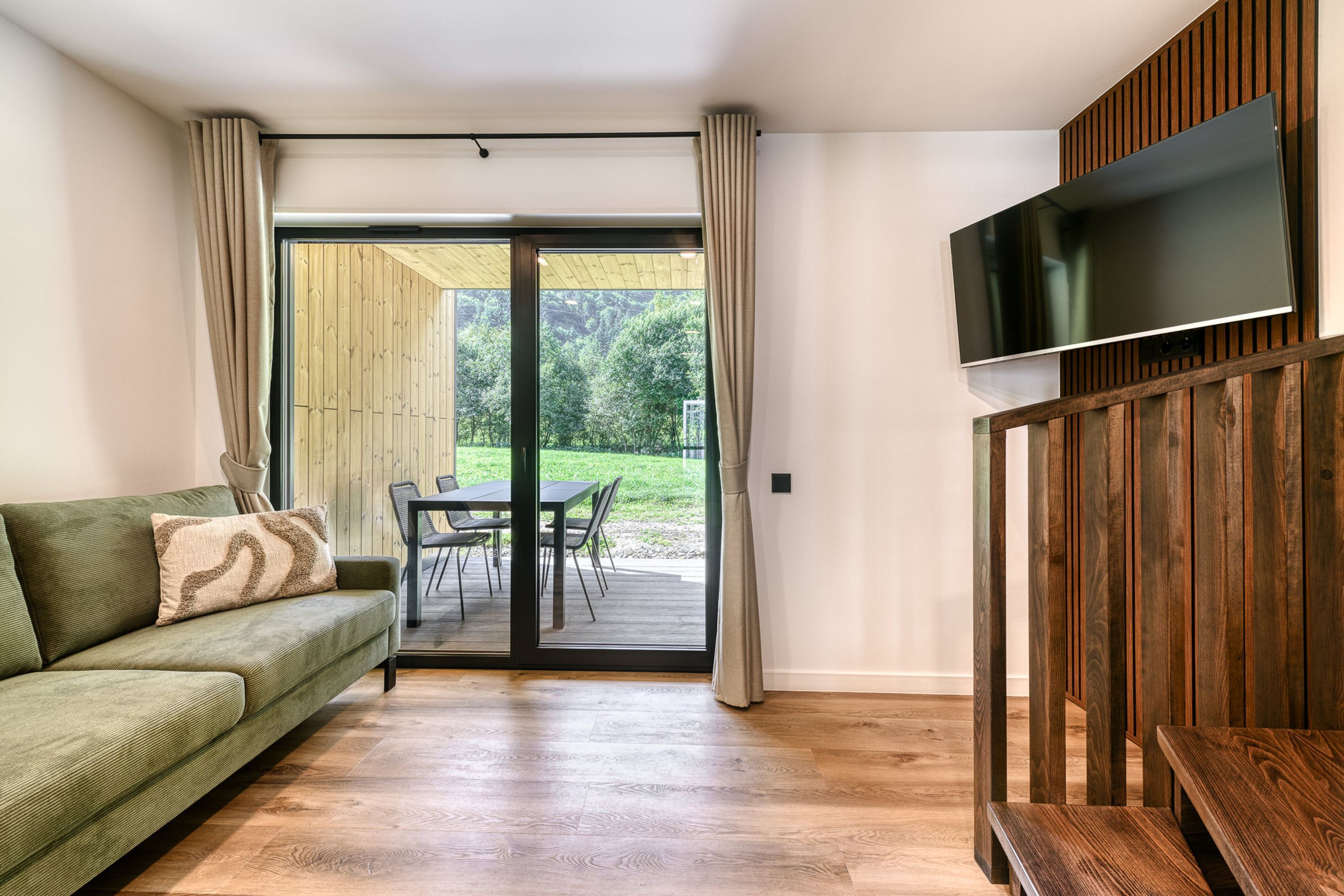 Una habitación con un sofá verde, una mesa de comedor de madera y un televisor montado en un panel de madera.
