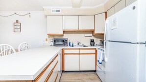 A compact kitchen with white cabinets, a microwave, a sink, and a refrigerator.