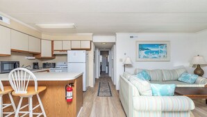 A compact living space with a kitchenette, a striped sofa, and a painting on the wall.
