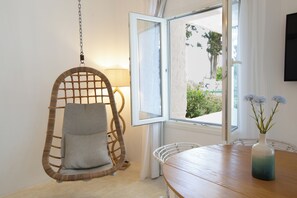 A room with a hanging chair, a table with a vase, and an open window. - Votsalo Sea Side (Andros)