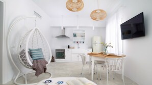 A modern, minimalist living space with a hanging chair, a dining area with a table and chairs, a kitchen, and a TV mounted on the wall. - Votsalo Sea Side (Andros)