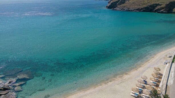 A beach with clear turquoise water, a sandy shore, and a rocky cliff. - Votsalo Sea Side (Andros)