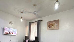 A living room with a sofa, a TV, a dining table with chairs, and a ceiling fan. - NYALI 1BR/Hot Shower/AC/Parking behind Quickmart (Mombasa)