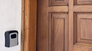 A wooden door with a rectangular panel design and a doorbell button on the adjacent wall. - NYALI 1BR/Hot Shower/AC/Parking behind Quickmart (Mombasa)