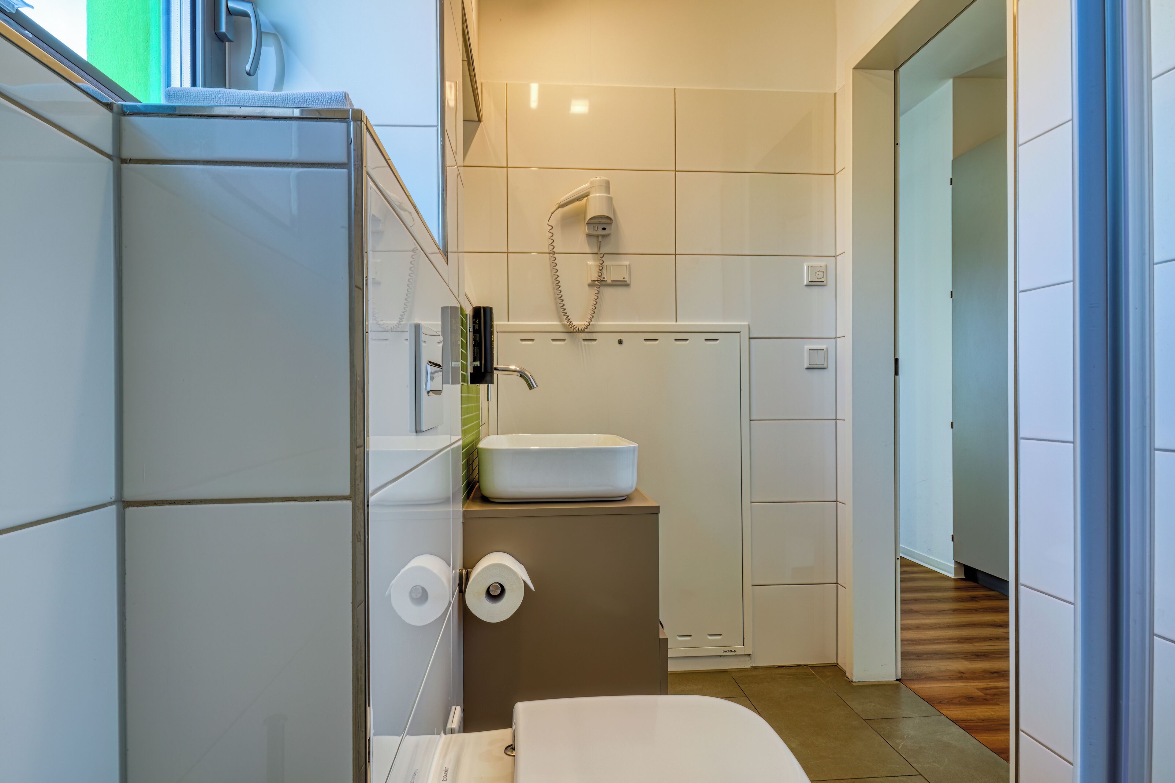 A compact bathroom with a toilet, sink, and a hairdryer mounted on the wall.