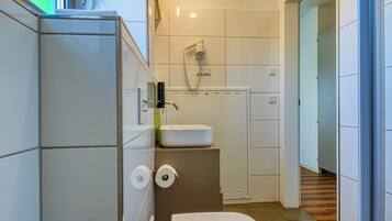A compact bathroom with a toilet, sink, and a hairdryer mounted on the wall.