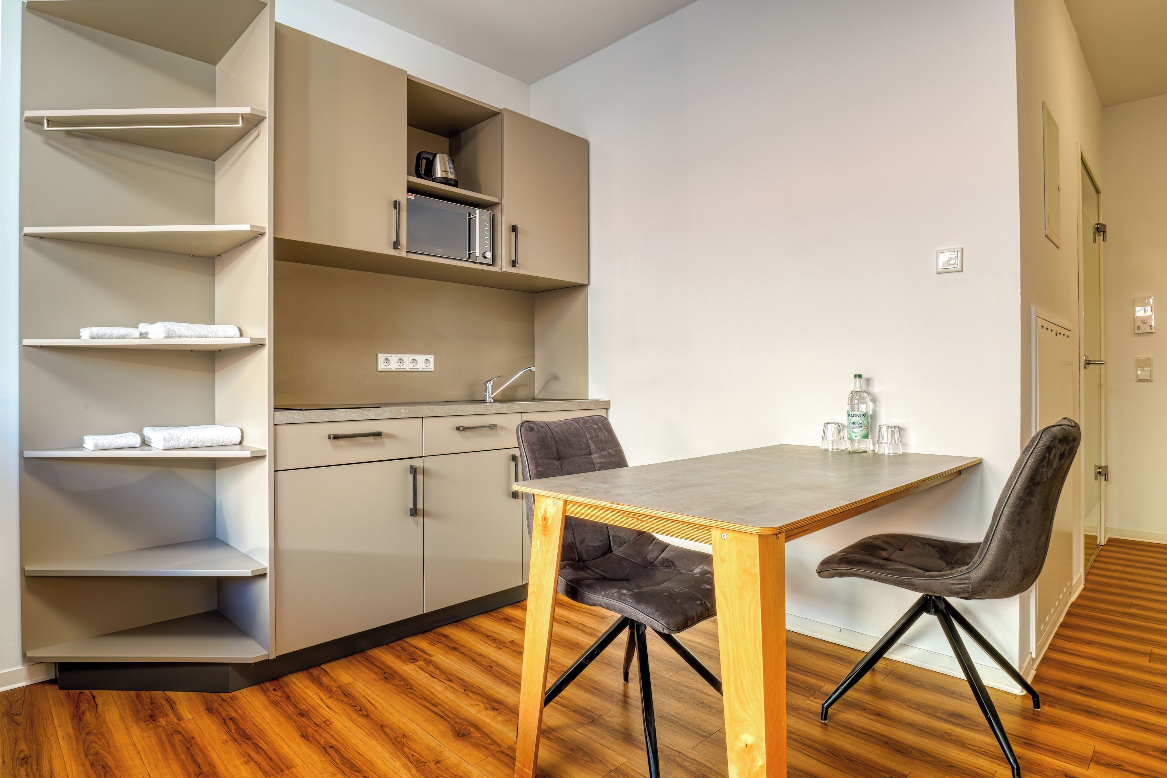 A modern kitchen with built-in shelves, a dining table with chairs, and a wooden floor.