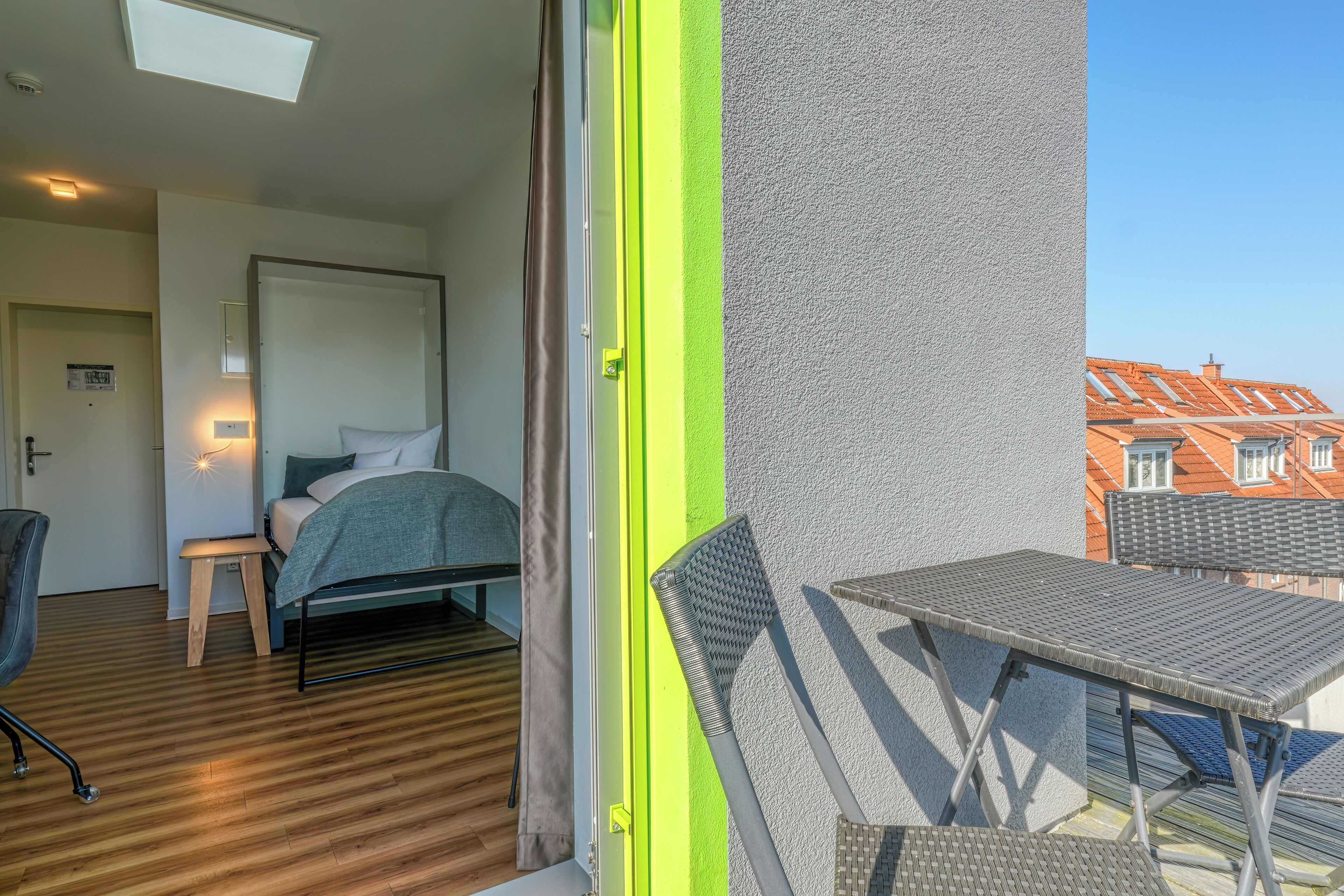 A hotel room with a bed, a small table, a chair, and a balcony with a table and chairs.