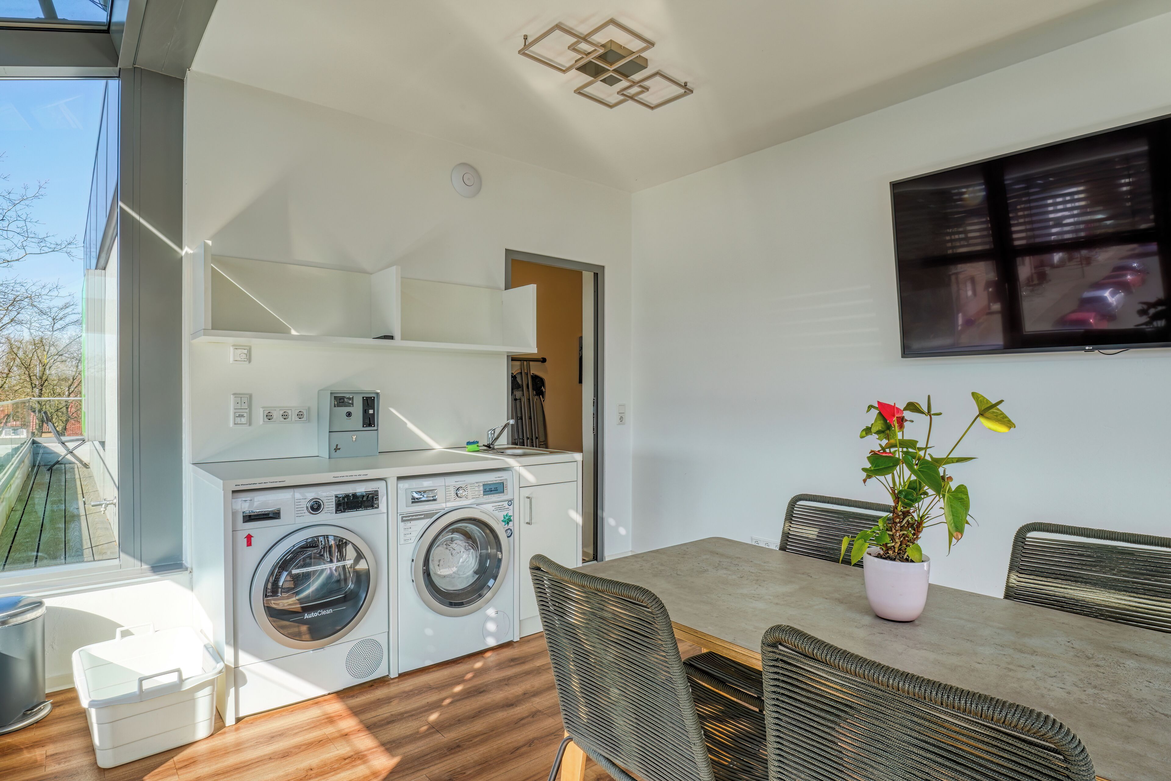 A compact kitchen with a washing machine, a dining table with chairs, and a potted plant.