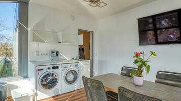 A compact kitchen with a washing machine, a dining table with chairs, and a potted plant.