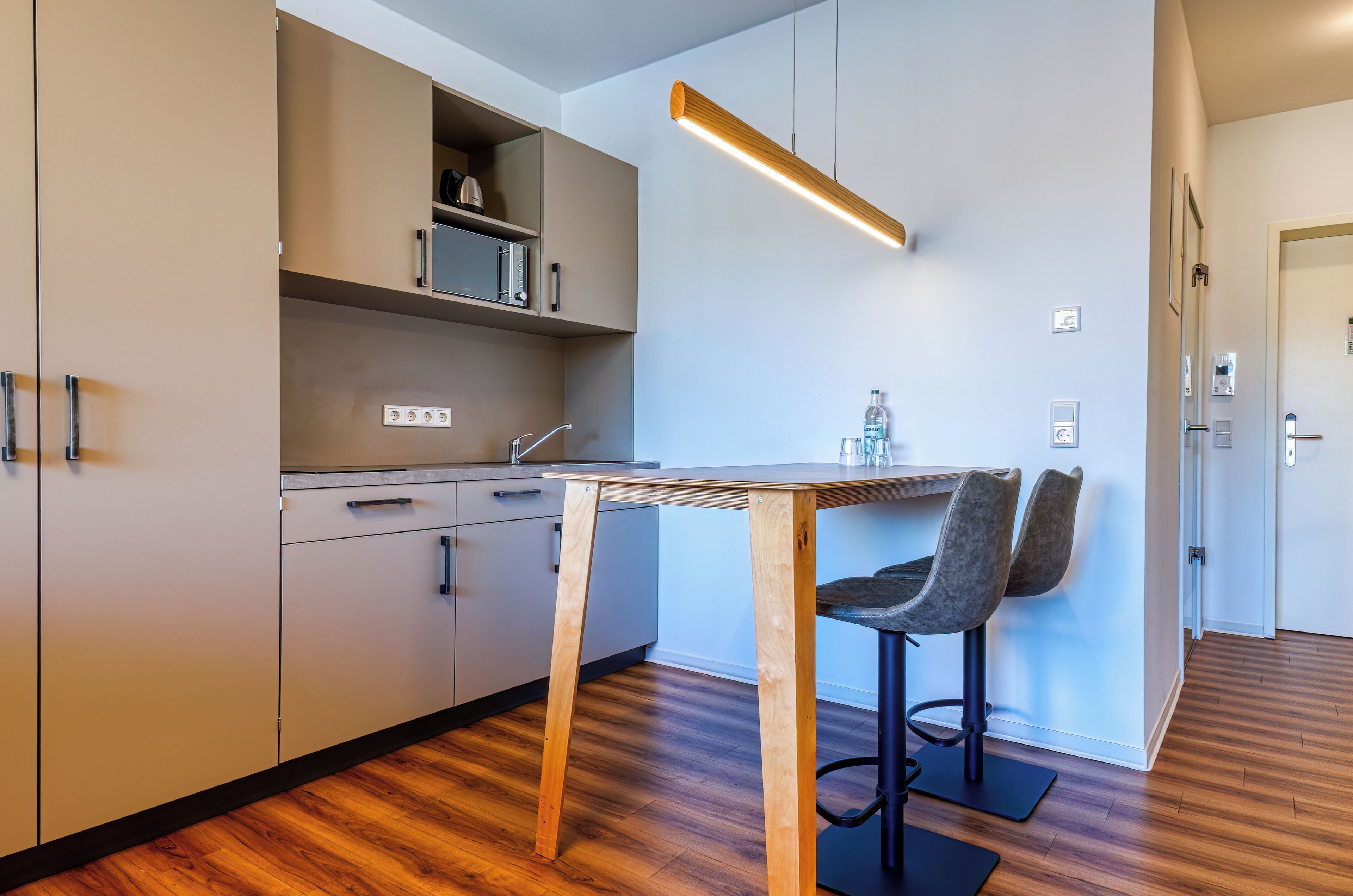 A modern kitchen with wooden flooring, a dining table with two chairs, and built-in cabinets.