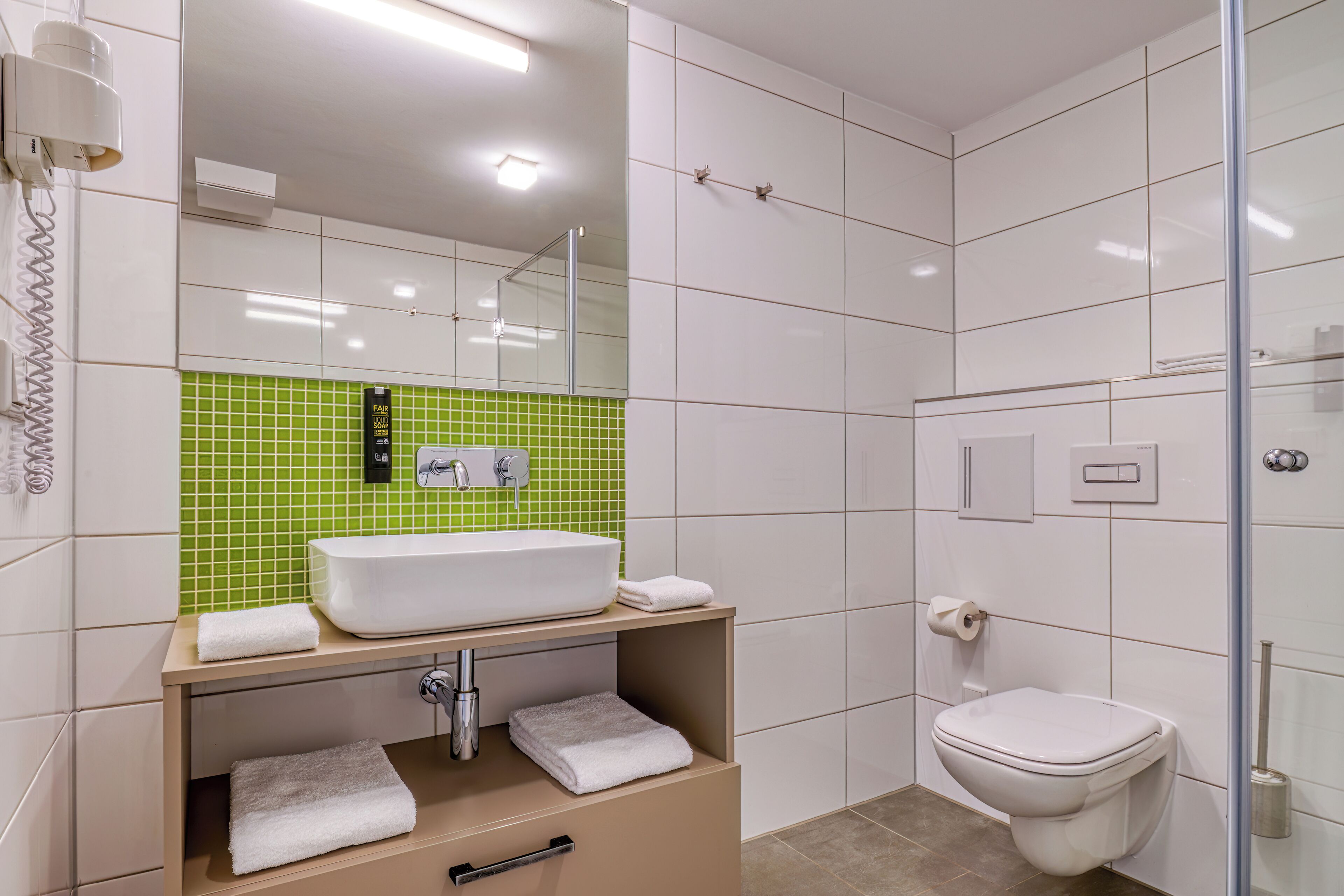 A modern bathroom with a white sink, green-tiled backsplash, and a glass shower enclosure.