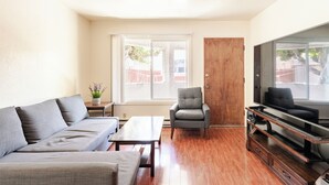 Een woonkamer met een bank, fauteuil, salontafel, tv-meubel en een deur.