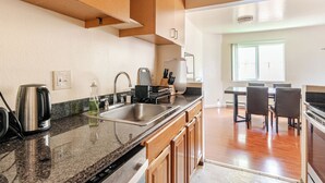 Een moderne keuken met granieten aanrechtbladen, roestvrijstalen apparatuur, houten keukenkastjes en een eethoek met een tafel en stoelen.