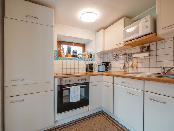 A compact kitchen with white cabinets, a stove, a microwave, and a window above the sink.
