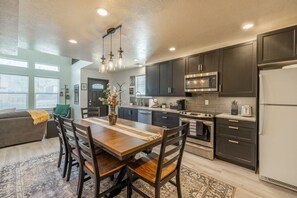 Une cuisine moderne avec des meubles de couleur sombre, des appareils en acier inoxydable et un coin repas comprenant une table et des chaises en bois.