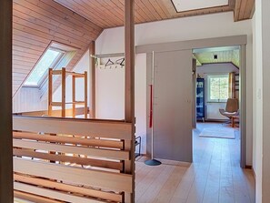 Une pièce dotée d’un plafond en pente, d’un plancher en bois, d’une banquette intégrée et d’une porte donnant sur une autre pièce avec une fenêtre et une chaise.