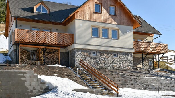 A multi-story wooden house with a stone foundation, a wooden balcony, and a staircase leading to the entrance.