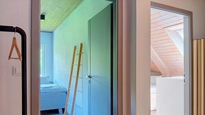 A room with a bed, a ladder, and a door leading to another room.