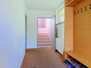 Un couloir doté d’un sol recouvert de moquette, d’un porte-chaussures en bois et d’un escalier menant à une autre pièce.