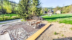 A wooden bench in a landscaped area with a stone pathway and a pile of firewood.