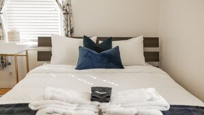 Una cama bien hecha con ropa blanca, una almohada azul oscuro y una toalla doblada sobre la cama.