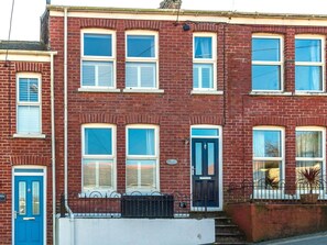 A red brick terraced house with a blue door and windows, a white front step, and a small black metal fence.