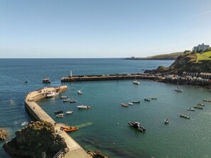 Un port côtier avec des bateaux, un phare et un bâtiment situé sur une colline.