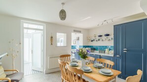 A dining area with a wooden table set for six, surrounded by wooden chairs. A vase with flowers is on the table. - Wonderful private villa for 6 guests with WIFI, TV, terrace and pets allowed (Mevagissey)