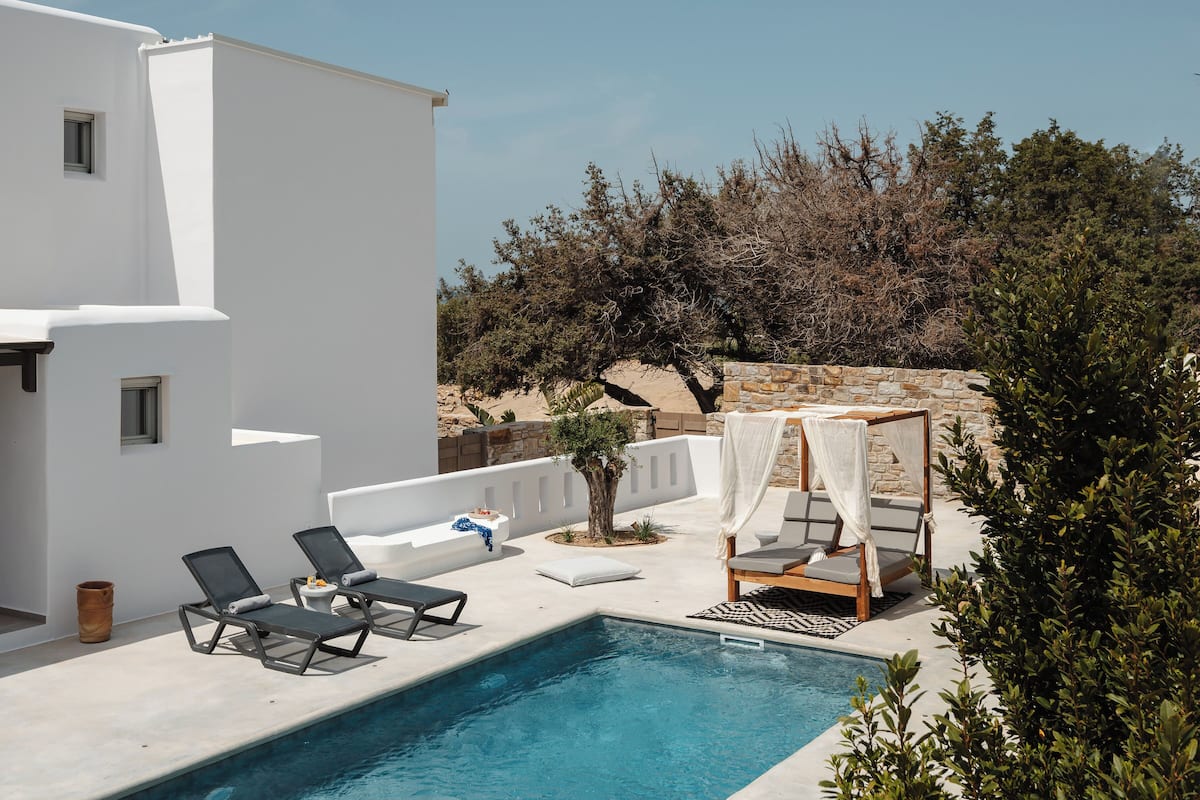 A pool area with lounge chairs, a wooden deck, and a white building.