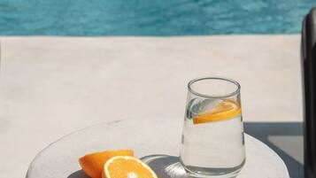 Un verre d’eau avec une tranche d’orange, posé sur une table en béton, près d’une piscine.