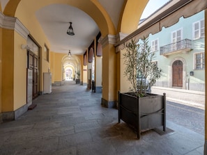 A corridor with arches, a potted plant, and a building with a balcony.