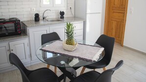 Una pequeña cocina con armarios blancos, un microondas, un lavamanos y un refrigerador. Hay una mesa de vidrio con cuatro sillas y una piña encima.