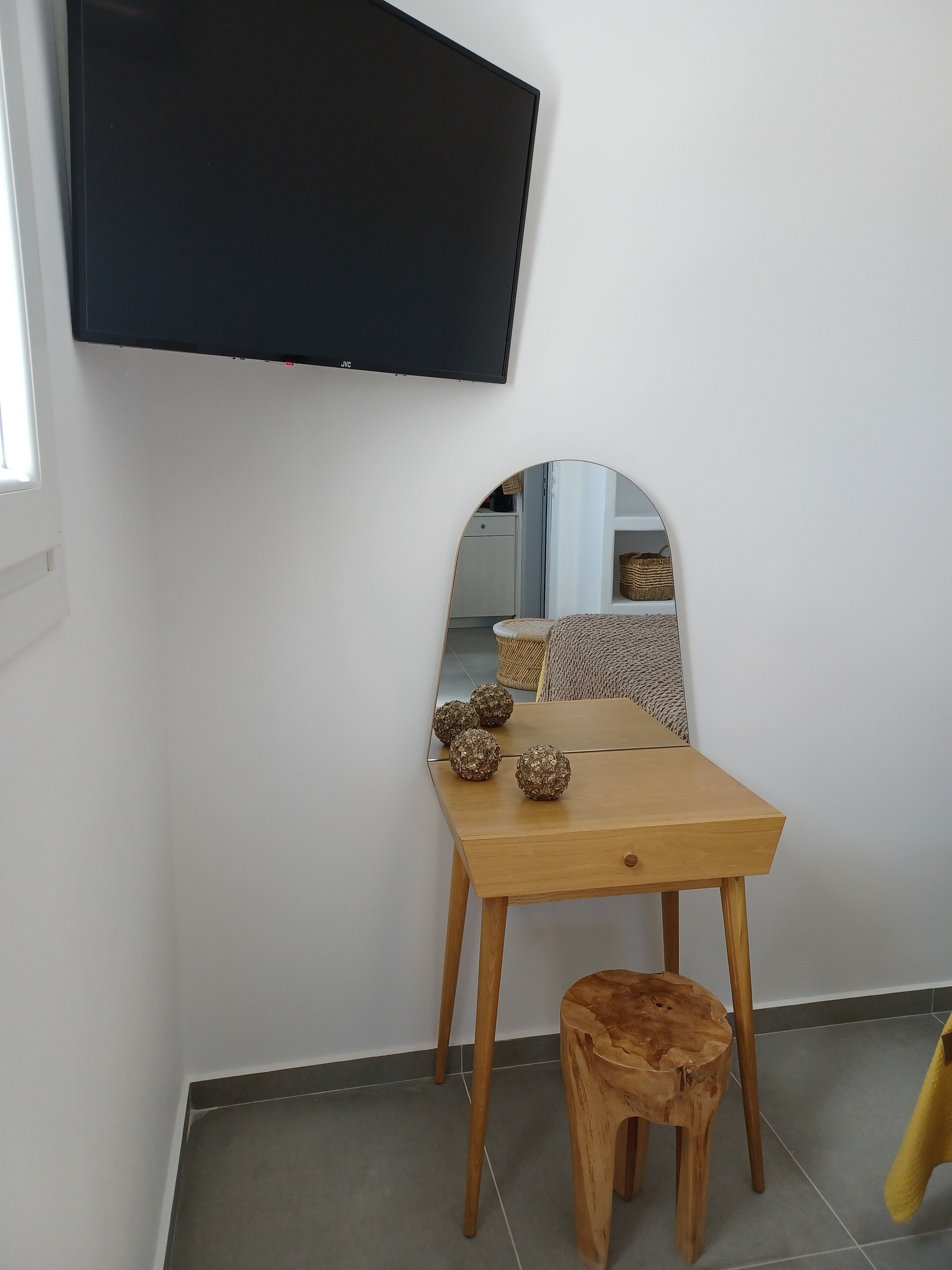 A room with a wooden table, a small stool, a mirror, and a flat-screen TV mounted on the wall.