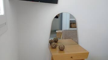 A room with a wooden table, a small stool, a mirror, and a flat-screen TV mounted on the wall.