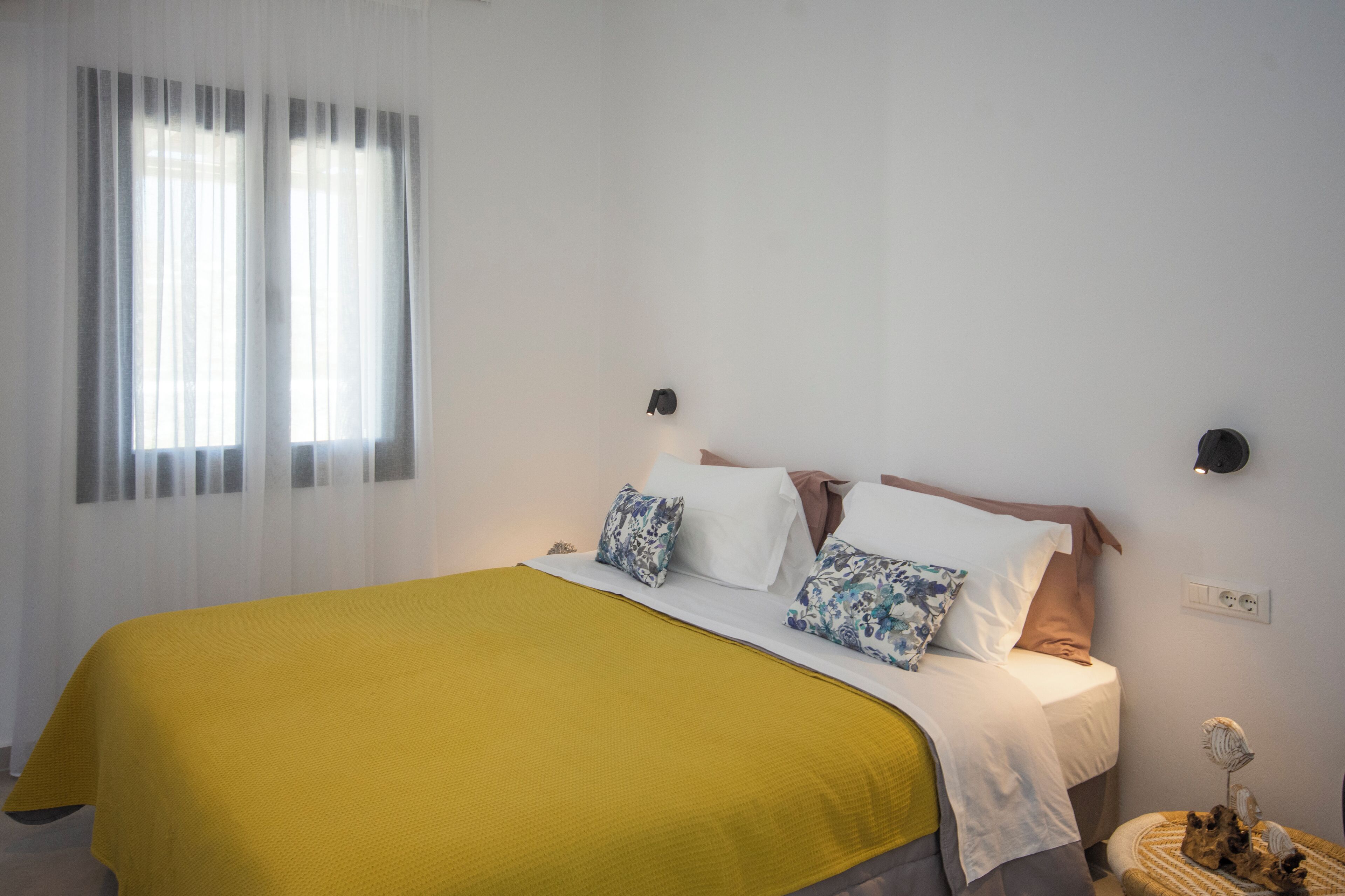 A neatly made bed with a yellow bedspread, white pillows, and a brown headboard. There are two wall-mounted nightstands with decorative items on them.