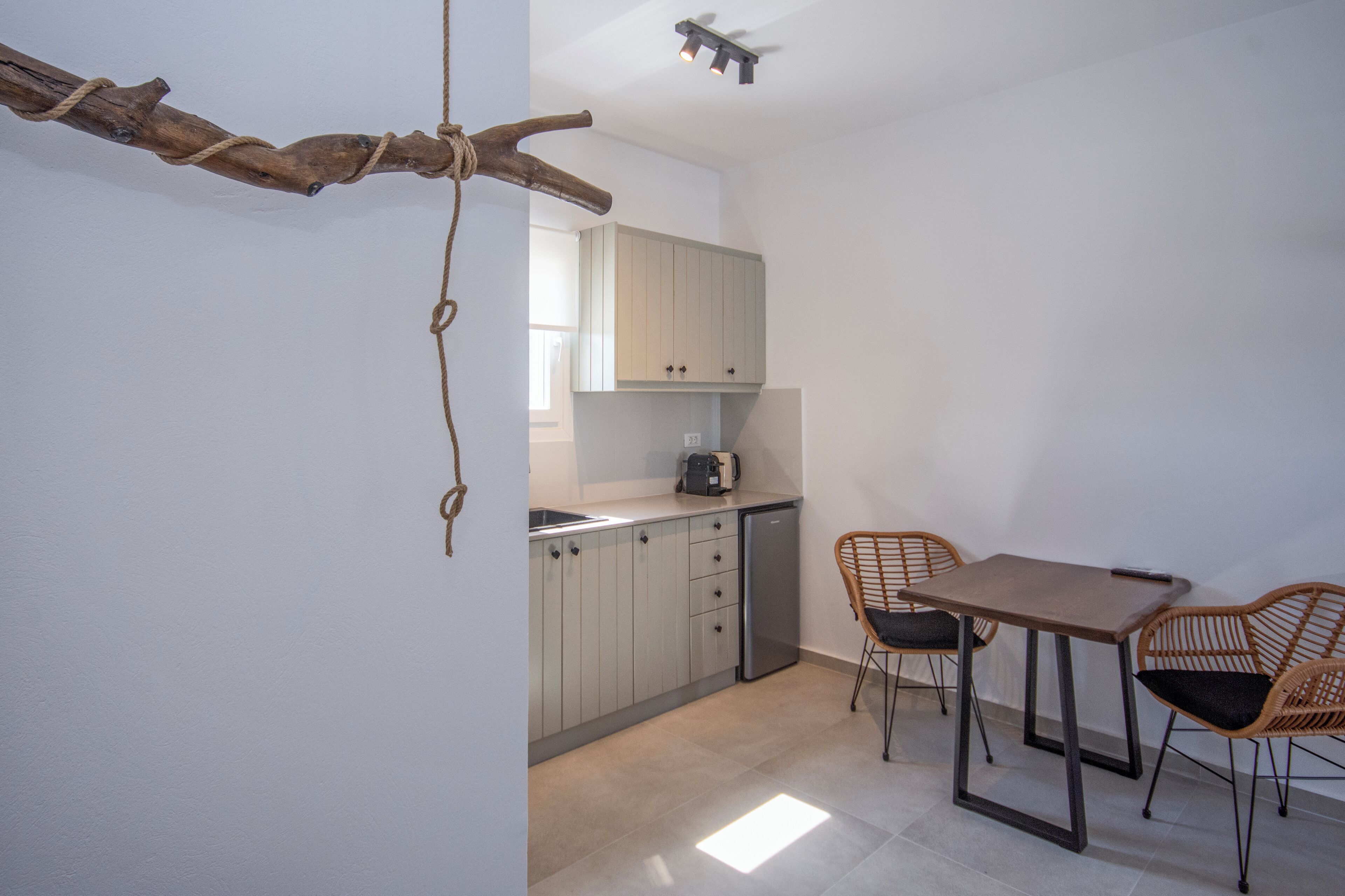 Cocina compacta con comedor, con una decoración de rama de madera, armarios de colores claros, un refrigerador pequeño y sillas de mimbre.