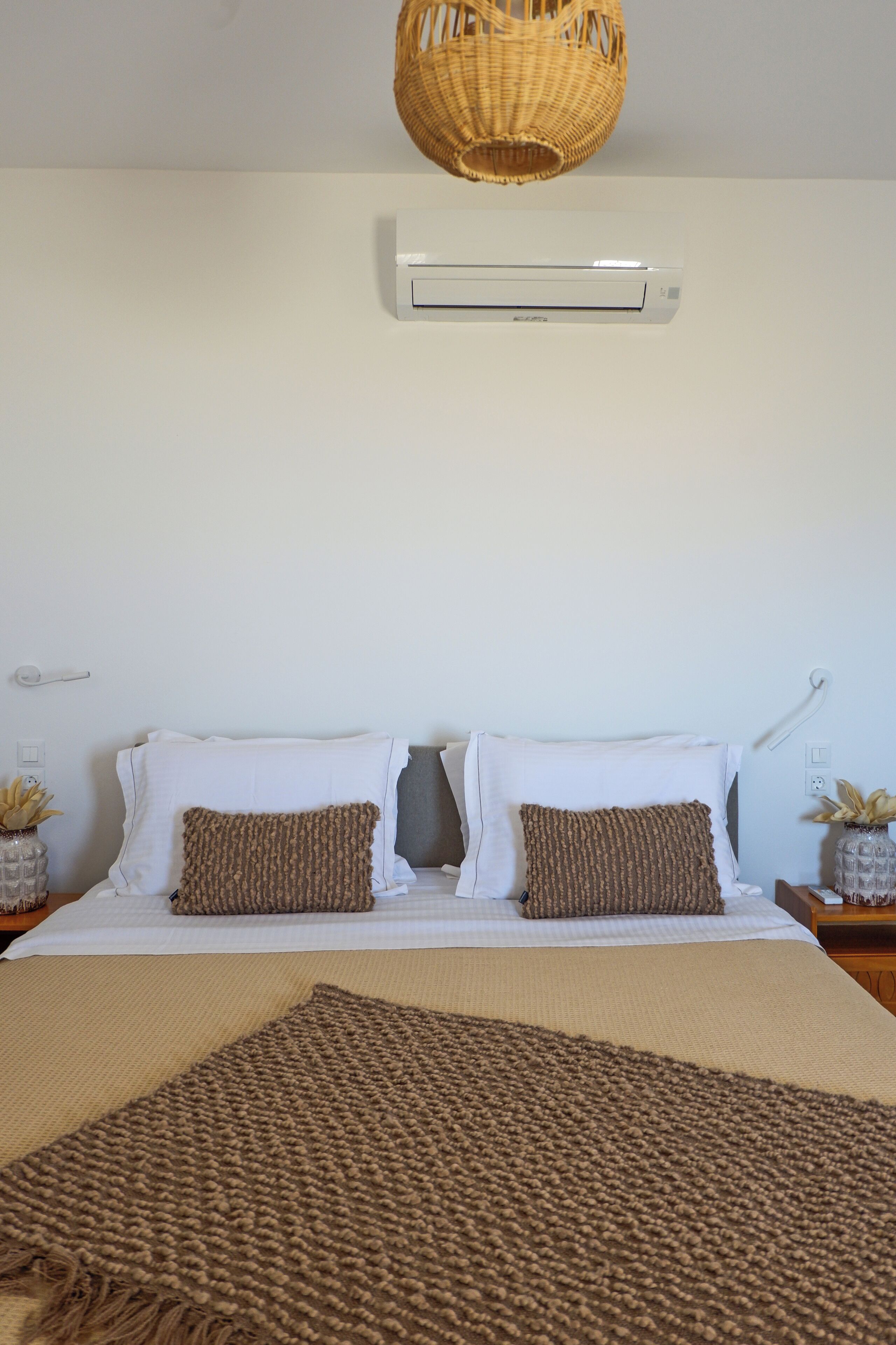 A neatly made bed with two pillows, a woven throw blanket, and a wall-mounted air conditioner above.