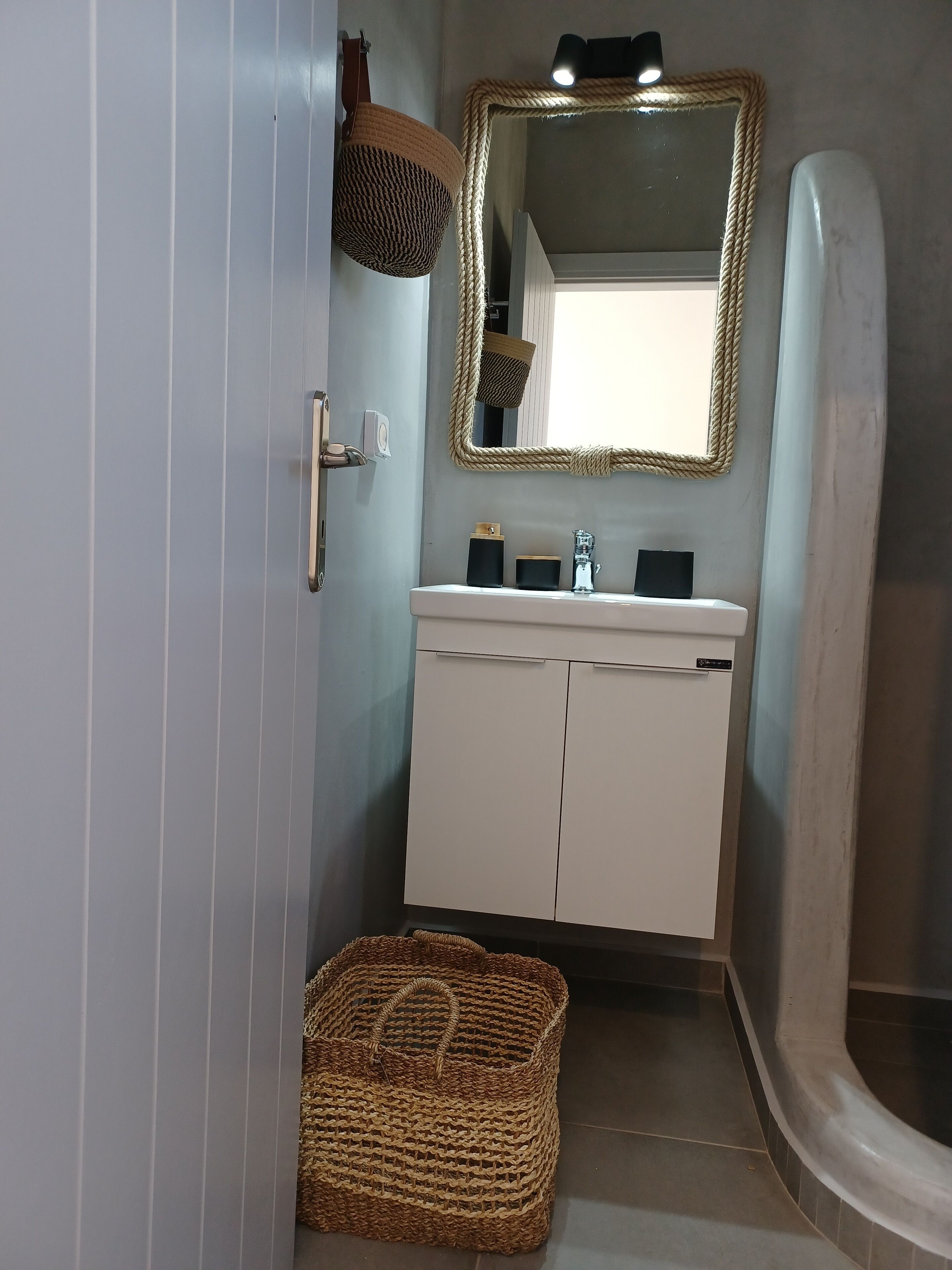 A bathroom with a white sink, a mirror with a rope frame, and a woven basket on the floor.