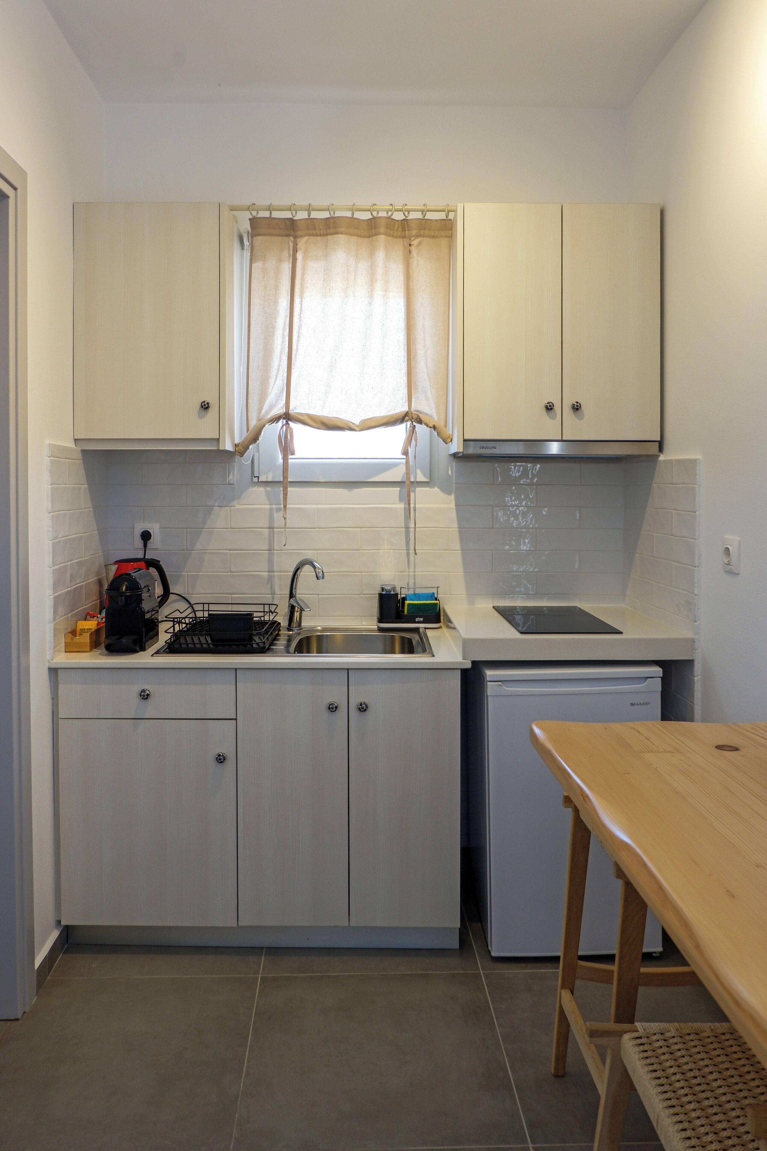Una cocina compacta con armarios blancos, un lavamanos, lavavajillas y una mesa de madera.