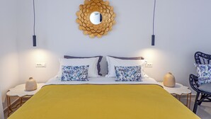 Un dormitorio ordenado con una cama grande, dos mesitas de noche, una silla y un espejo colgado en la pared.