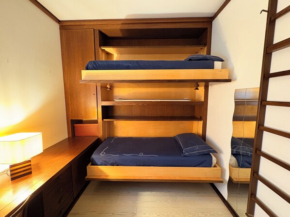 A bunk bed with a desk and drawers underneath, a lamp on the desk, and a ladder to the right.