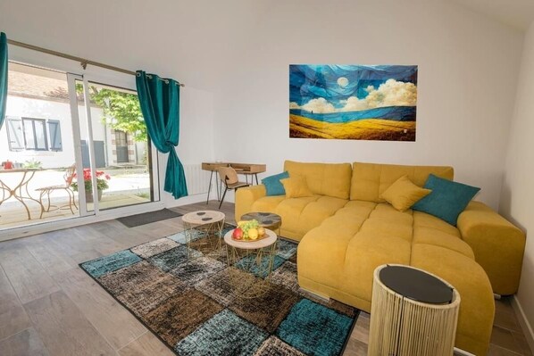 A living room with a yellow sofa, a painting of a landscape, and a view through large glass doors. - Le domaine de Darvoy (Darvoy)